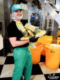Person in a BjornQorn popcorn processing plant holding bags of popcorn and wearing a green cap.
