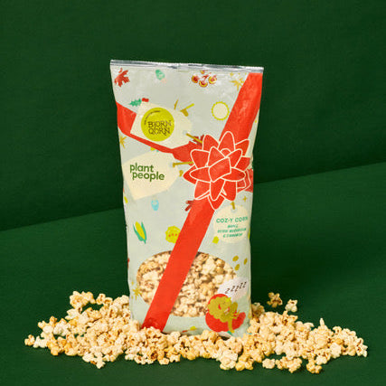 Popcorn bag with red bow and popcorn spilling out on a green background